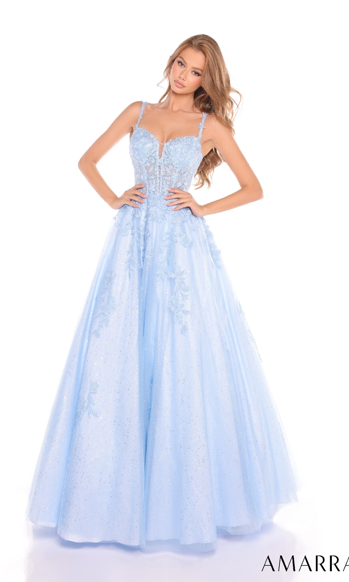 A woman wears the Amarra 88590 Floral Lace Prom Ball Gown, a light blue, floor-length tulle dress with glitter, a fitted bodice, lace details, thin straps, and an elegant, full silhouette.